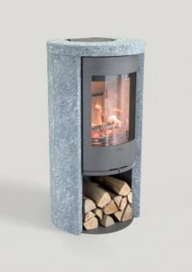Modern braskamin i grå sten med synlig eld och vedförvaring undertill, mot en ljus bakgrund. Perfekt för hemuppvärmning och stilfull inredning.