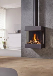 Väggmonterad modern öppen spis med brinnande ved, i ett ljust vardagsrum med trägolv och grå vägg.