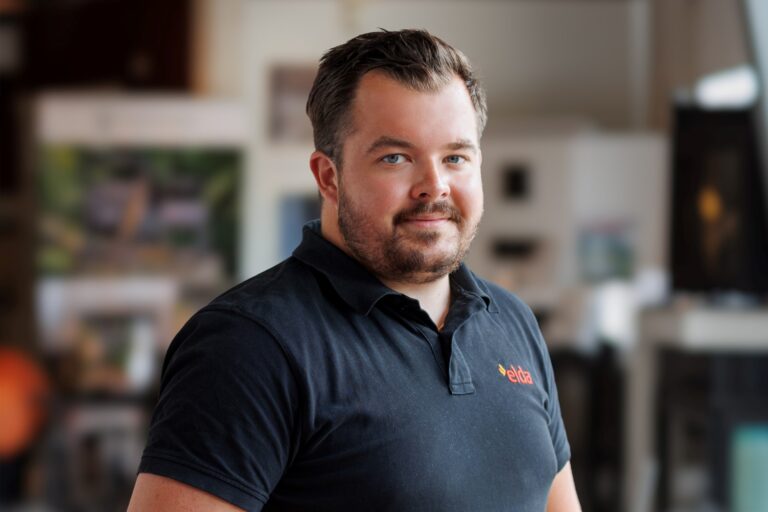 Man i svart Eldabutiken-tröja står inomhus med suddig bakgrund. Porträttbild för användning på Eldabutikens webbplats.