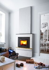 Vit inomhusmiljö med en modern eldstad. Elden brinner klart. Lekbil och leksaker på golvet. Matplats synlig i bakgrunden. Mysig och stilren atmosfär.