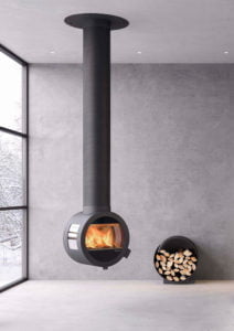Modern, väggmonterad svart kamin med brinnande eld, bredvid en vedförvaringsenhet fylld med vedträn, i ett rum med stora fönster och betongväggar.