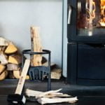 Vedklyvningsverktyg med vedträ och hammare framför en brinnande kamin, omgiven av staplad ved. Perfekt för effektiv vedhantering vid eldstaden.