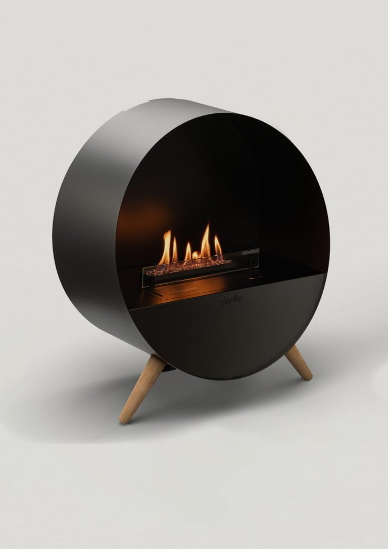 Svart, rund elektrisk kamin av märket Planika med synliga lågor, placerad på träben, mot en neutral bakgrund.