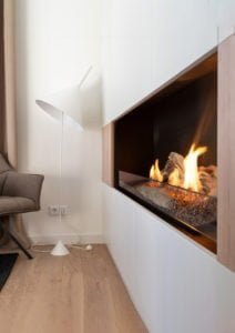 Modern inredning med en elegant golvlampa, bekväm fåtölj och stilren väggmonterad eldstad med levande lågor. Perfekt för en mysig atmosfär.