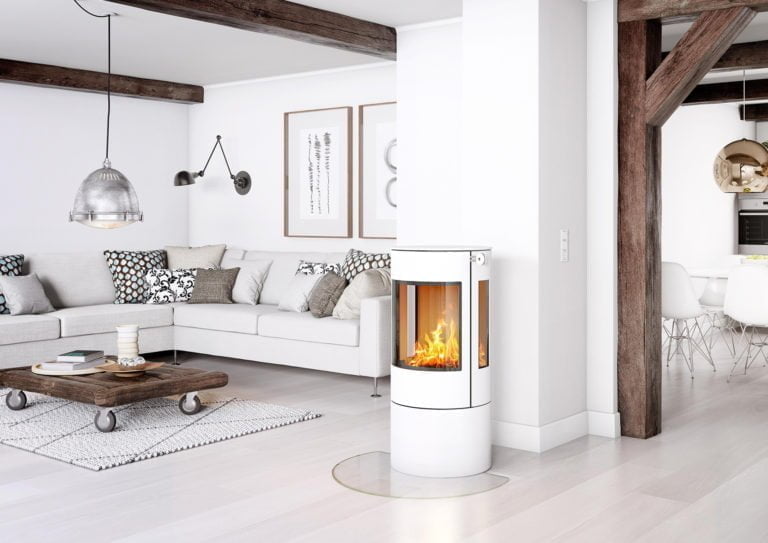 Modernt vardagsrum med vit kamin, grå soffa och träbord på hjul. Elden brinner i kaminen. Ljusa väggar och takbjälkar i trä.