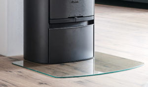 Svart kamin på trägolv, placerad på en skyddande glasplatta. Kaminen är enkel och modern i design.