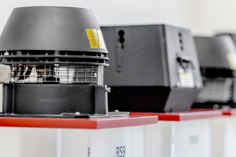 Svart ventilationsfläkt på röd bas, placerad på en vit bakgrund. Flera liknande enheter syns i bakgrunden.
