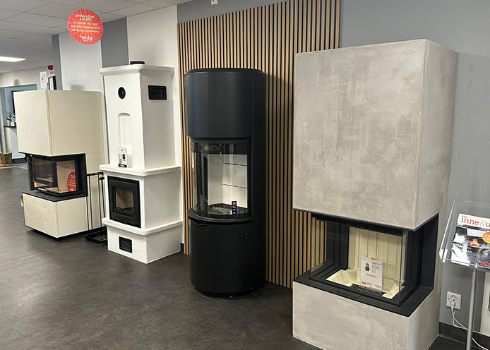 Utställning av fyra moderna kaminer i olika stilar och färger i en butiksmiljö med grått golv och ljusa väggar.